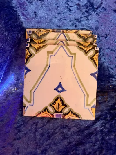 portugisiske azulejos eller marokkanske zellige-inspirerede fliser med et lyst felt og håndmalede motiver i gul, grøn, blå og lilla nuancer.