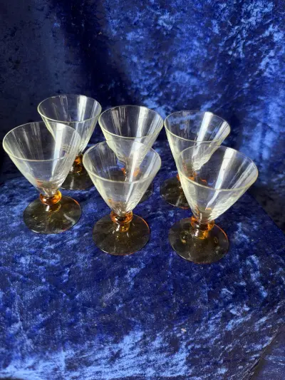 Portvins- eller likørglas med ravfarvet fod, der stilmæssigt og visuelt ligner klassisk dansk glaskunst fra midten af det 20. århundrede, såsom Holmegaards eller Kastrup Glasværks elskede modeller med
